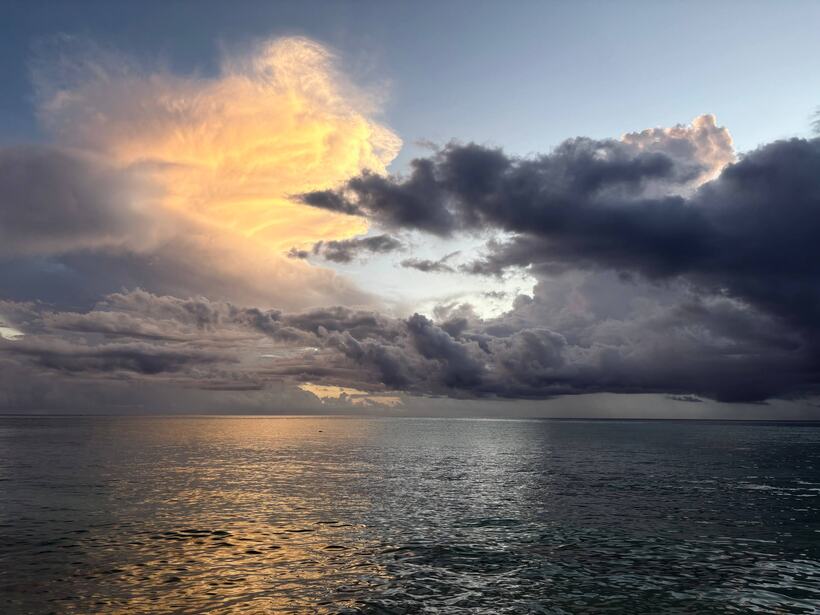 A single tall cloud lit gold by the setting sun above a calm sea, heavy dark cloud to the right