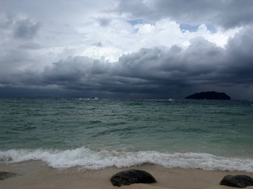 A dark storm front over a green sea, boulders on the sand in the foreground, an island on the horizon