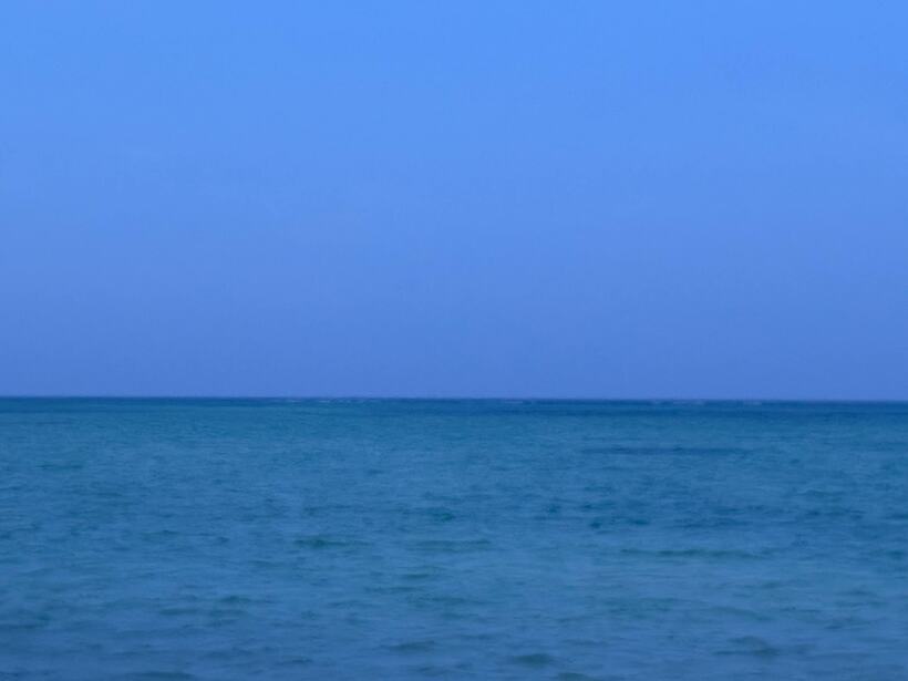 A minimal frame: flat blue sea below an even blue sky, the horizon a single line
