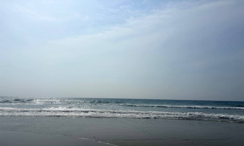Pale overcast light over a calm sea with a low line of surf running up the sand