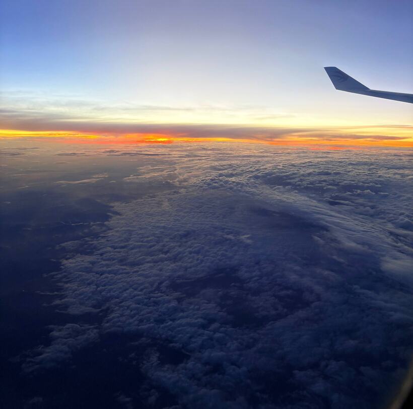 From an aircraft window: a wingtip above an unbroken floor of cloud, a pale band of sky at the horizon