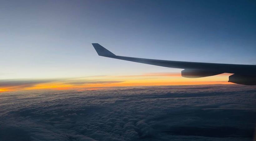 A jet wing above a cloud deck with a thin orange band of dawn along the horizon