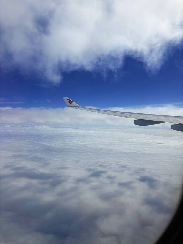 A jet wing over towering white cumulus under a deep blue sky